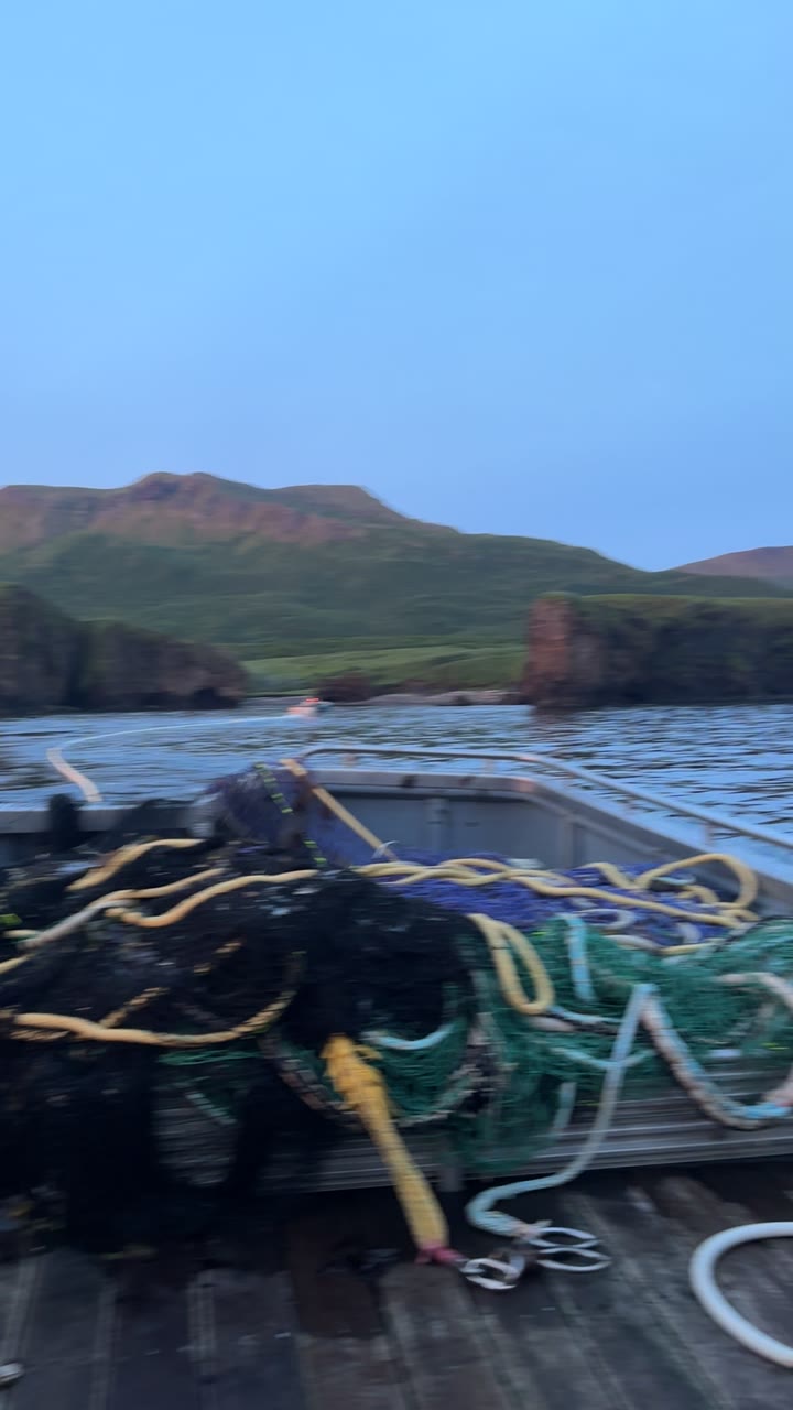 Stacked seine net, ropes and floats on deck with rocky cliffs of Popof at dusk